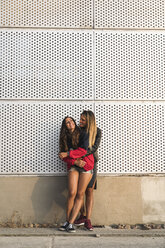 Glückliches lesbisches Paar, das sich an einer Wand umarmt - KKAF02492
