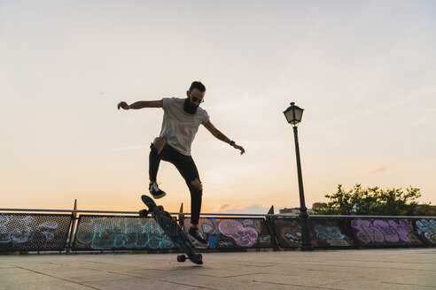 Junger Mann macht einen Skateboardtrick in der Stadt bei Sonnenuntergang - KKAF02516