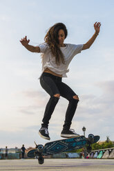 Junge Frau macht einen Skateboardtrick in der Stadt - KKAF02520