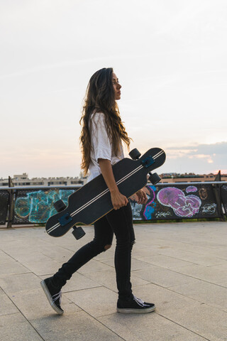 Junge Frau zu Fuß mit Skateboard in der Stadt, lizenzfreies Stockfoto