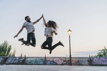 Exuberant couple jumping outdoors high fiving - KKAF02527