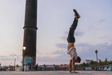 Young man doing a handstand in the city at sunset - KKAF02528