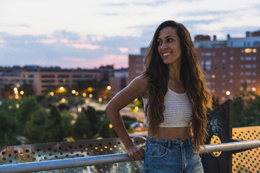 Beautiful smiling young woman with long brown hair in the city at dusk - KKAF02532