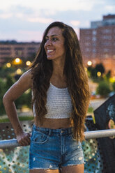 Beautiful smiling young woman with long brown hair in the city at dusk - KKAF02533