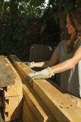 Smiling craftswoman wearing protective gloves working with wood - JPTF00039