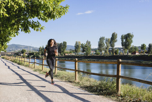 Sportliche junge Frau beim Laufen am Flussufer - FMOF00382