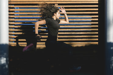 Sportive young woman running along wood paneling - FMOF00389