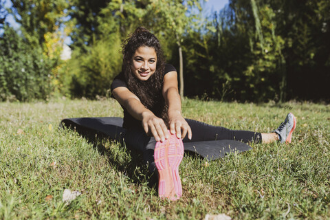 Sportliche junge Frau streckt ihr Bein auf einer Wiese, lizenzfreies Stockfoto