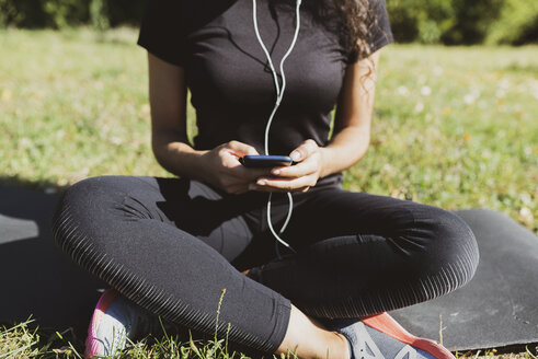 Sportliche junge Frau macht eine Pause auf einer Wiese und benutzt dabei ein Mobiltelefon - FMOF00394
