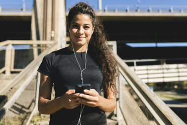 Portrait of sporty young woman having a break listening to music - FMOF00401