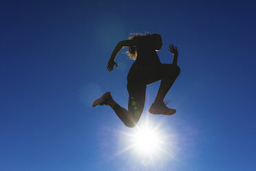 Sportliche junge Frau springt unter blauem Himmel im Gegenlicht - FMOF00406