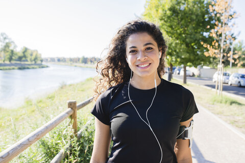 Porträt einer lächelnden, sportlichen jungen Frau am Flussufer, lizenzfreies Stockfoto