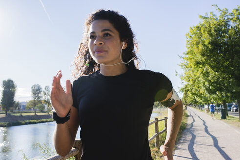 Sportliche junge Frau beim Laufen am Flussufer - FMOF00414