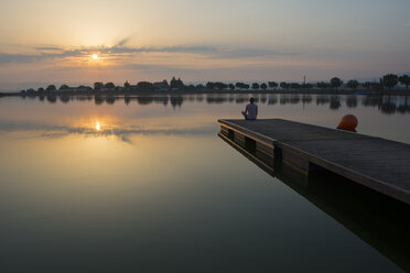 Entspanntes Mädchen auf der schwimmenden Plattform auf dem See bei Sonnenaufgang - SKCF00550