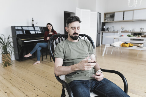 Couple at home, Man drinking wine, woman playing he piano in background stock photo