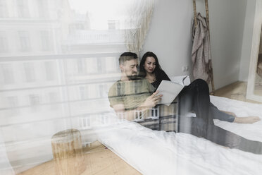 Couple sitting on bed, flipping through a book - KMKF00585
