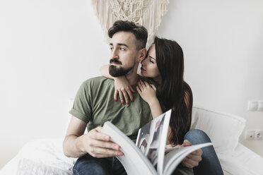 Couple sitting on bed, flipping through a book - KMKF00586