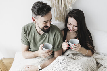 Happy couple sitting in bed, drinking coffee, having fun - KMKF00590