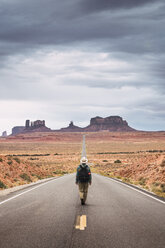 USA, Utah, Man with backpack walking on road to Monument Valley - KKAF02540