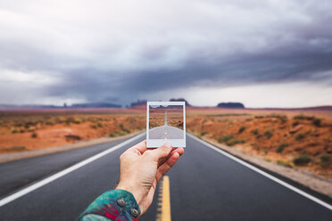 USA, Utah, Hand hält Instagram-Foto über Straße nach Monument Valley - KKAF02543