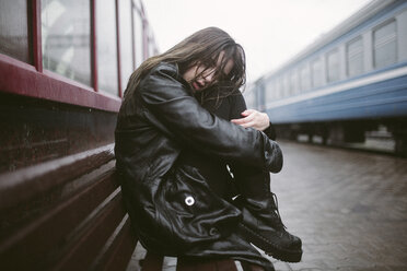 Porträt einer traurigen Frau, die während der Regenzeit auf einer Bank am Bahnhof sitzt - CAVF50470