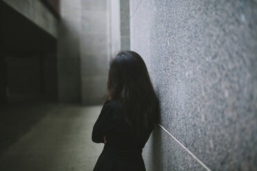 Rear view of woman standing by tiled wall - CAVF50471