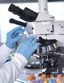 Abgeschnittene Hände eines männlichen Wissenschaftlers, der einen Objektträger mit Blut unter einem Mikroskop im Labor hält - CAVF50477