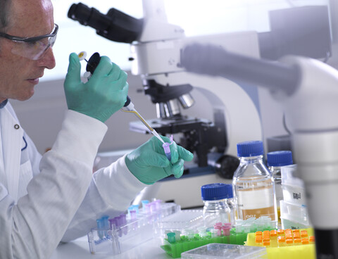 Männlicher Wissenschaftler beim Pipettieren von Proben in einem Fläschchen auf einem Tisch im Labor, lizenzfreies Stockfoto