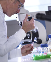 Seitenansicht eines männlichen Wissenschaftlers, der Proben in ein Fläschchen auf einem Tisch im Labor pipettiert - CAVF50482