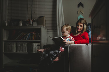 Mutter mit Sohn, der auf einem Sessel zu Hause sitzt und ein Buch liest - CAVF50484