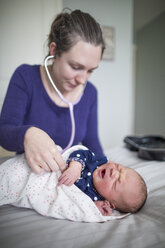 Hebamme bei der Untersuchung eines neugeborenen Mädchens mit Stethoskop auf einem Bett zu Hause - CAVF50518