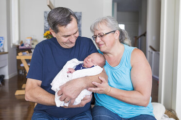 Grandparents with cute newborn granddaughter sitting in living room at home - CAVF50520