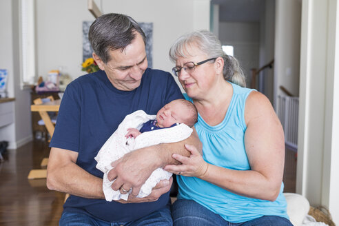 Großeltern mit süßer neugeborener Enkelin im Wohnzimmer zu Hause sitzend - CAVF50520