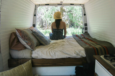Rückansicht einer Frau, die auf dem Bett eines Wohnmobils sitzend Bäume betrachtet - CAVF50524