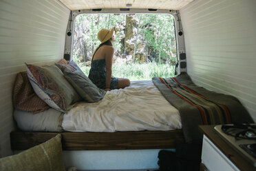 Seitenansicht einer Frau, die auf dem Bett eines Wohnmobils sitzend Bäume betrachtet - CAVF50525