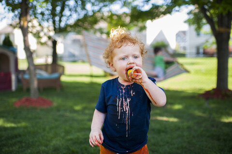 Niedlicher kleiner Junge isst Eis, während er auf einer Wiese im Hof steht, lizenzfreies Stockfoto