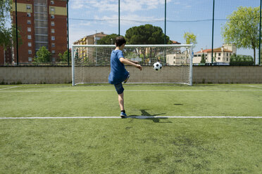 Rückansicht eines Jungen, der einen Fußball gegen ein Netz auf einem Spielfeld tritt - CAVF50547