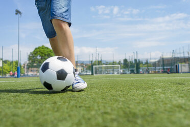 Low section of boy practicing soccer on field against sky - CAVF50551