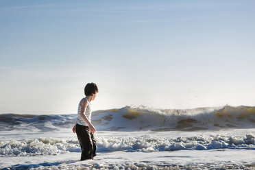 Seitenansicht eines Jungen, der mit den Wellen spielt, während er im Meer steht, gegen den Himmel bei Sonnenuntergang - CAVF50567