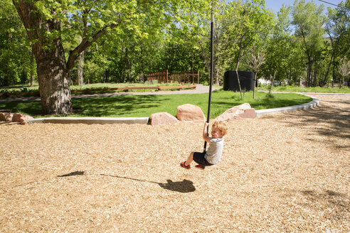 Junge in voller Länge auf Seilrutsche auf Spielplatz im Sommer sitzend - CAVF50568