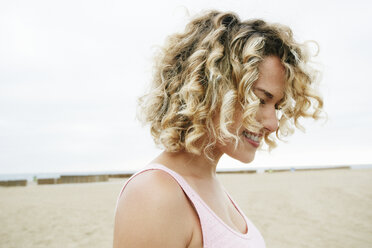 Porträt einer lächelnden jungen Frau mit blondem, lockigem Haar am Sandstrand. - MINF09086
