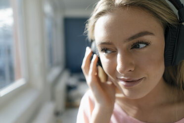 Smiling young woman listening music at home - KNSF05006