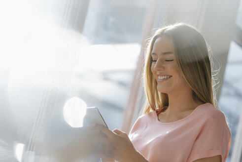 Porträt einer lachenden jungen Frau, die auf ihr Mobiltelefon schaut - KNSF05025