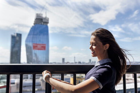 UK, London, lächelnde Frau mit Smartwatch auf einer Dachterrasse - MGOF03808