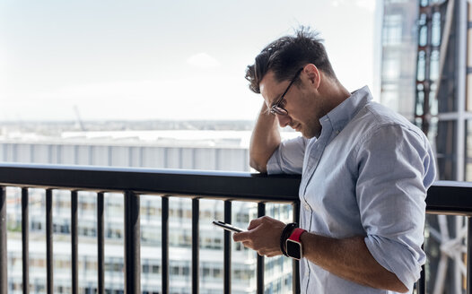 UK, London, Mann benutzt Mobiltelefon auf einer Dachterrasse - MGOF03812