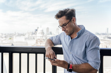 UK, London, Mann benutzt Mobiltelefon auf einer Dachterrasse - MGOF03819