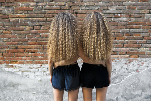 Back view of twin sisters with ringlets standing arm in arm side by side - GIOF04718