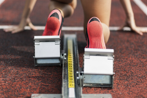 Teenage runner kneeling on starting block, close up stock photo