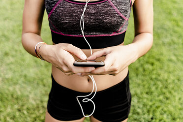 Teenage girl using smartphone and earphone on race track - GIOF04804