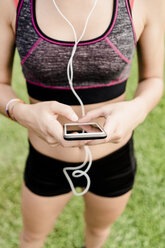 Teenage girl using smartphone and earphone on race track - GIOF04805